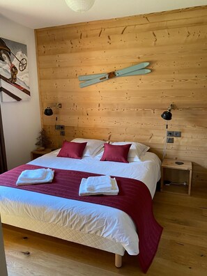 Un dormitorio con cabecera de madera, una cama con ropa de cama blanca y roja, dos mesitas de noche con lámparas y una lámpara de pared.