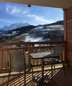Una terraza de madera con dos mesas y sillas, con vista a un paisaje nevado de montañas.
