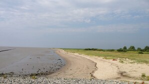 A beach with a rocky shoreline and a grassy area in the background. - Holiday homes and Apartments in the heart of Greetsiel, modern, comfortable + cozy, Internet (Greetsiel)