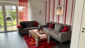 A modern living room with two grey sofas, a wooden coffee table, and a red and black checkered rug. - Holiday homes and Apartments in the heart of Greetsiel, modern, comfortable + cozy, Internet (Greetsiel)