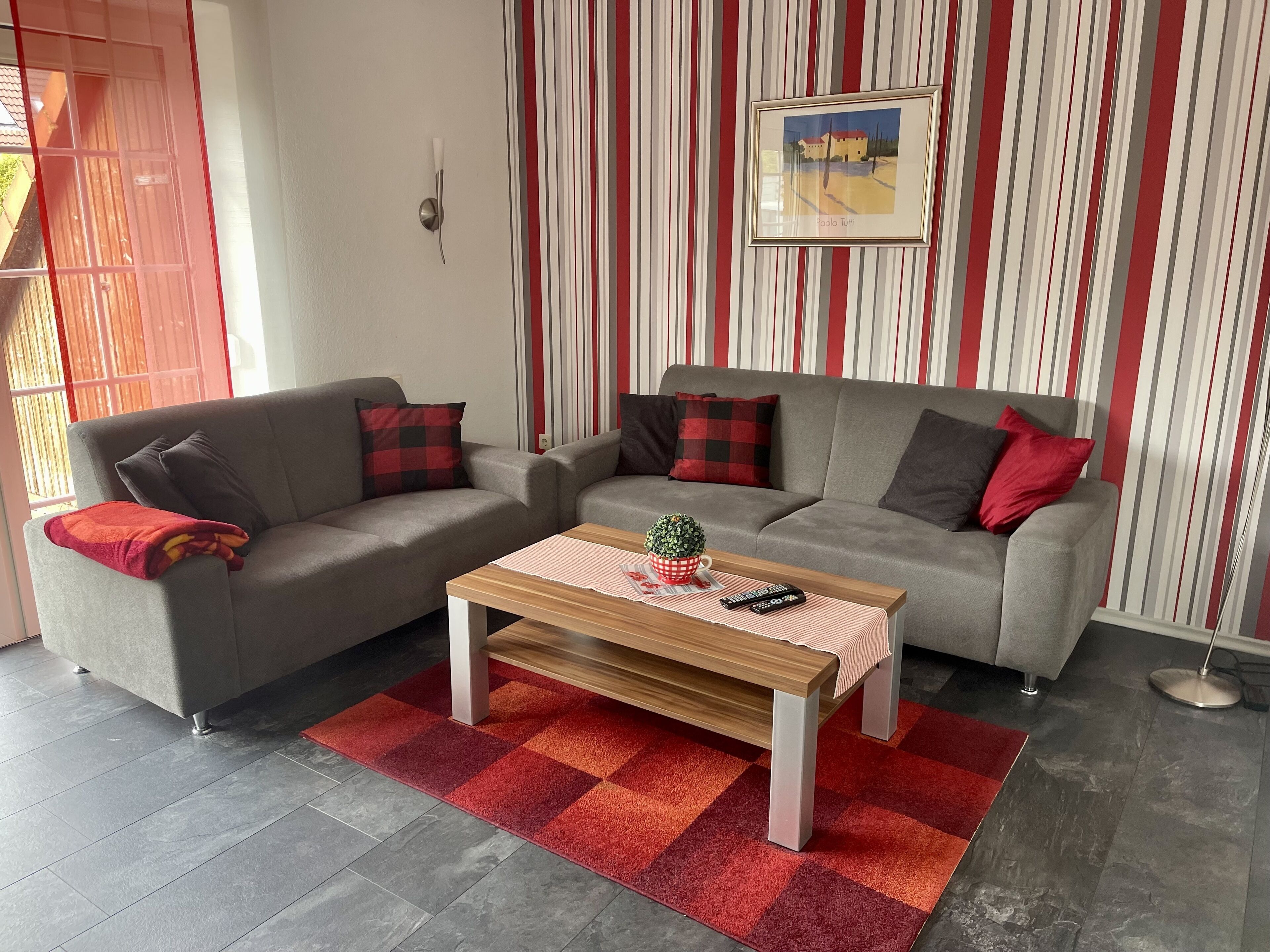 Un salon avec deux canapés gris, une table basse en bois et un tapis à carreaux rouges et oranges.