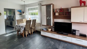 A modern living room with a dining area, a TV, and a kitchen visible through an open door. - Holiday homes and Apartments in the heart of Greetsiel, modern, comfortable + cozy, Internet (Greetsiel)