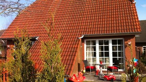 A house with a red tiled roof, a brick exterior, and a front porch with outdoor furniture. - Holiday homes and Apartments in the heart of Greetsiel, modern, comfortable + cozy, Internet (Greetsiel)