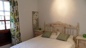 Een slaapkamer met een houten bed, twee nachtkastjes, een wanddecoratie en een raam met bloemen gordijnen.
