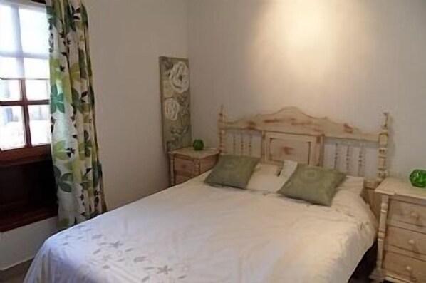 Een slaapkamer met een houten bed, twee nachtkastjes, een wanddecoratie en een raam met bloemen gordijnen.