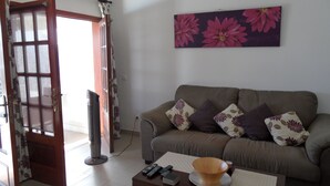 Een woonkamer met een bank, een flatscreen televisie, een salontafel en een deur met gordijnen.