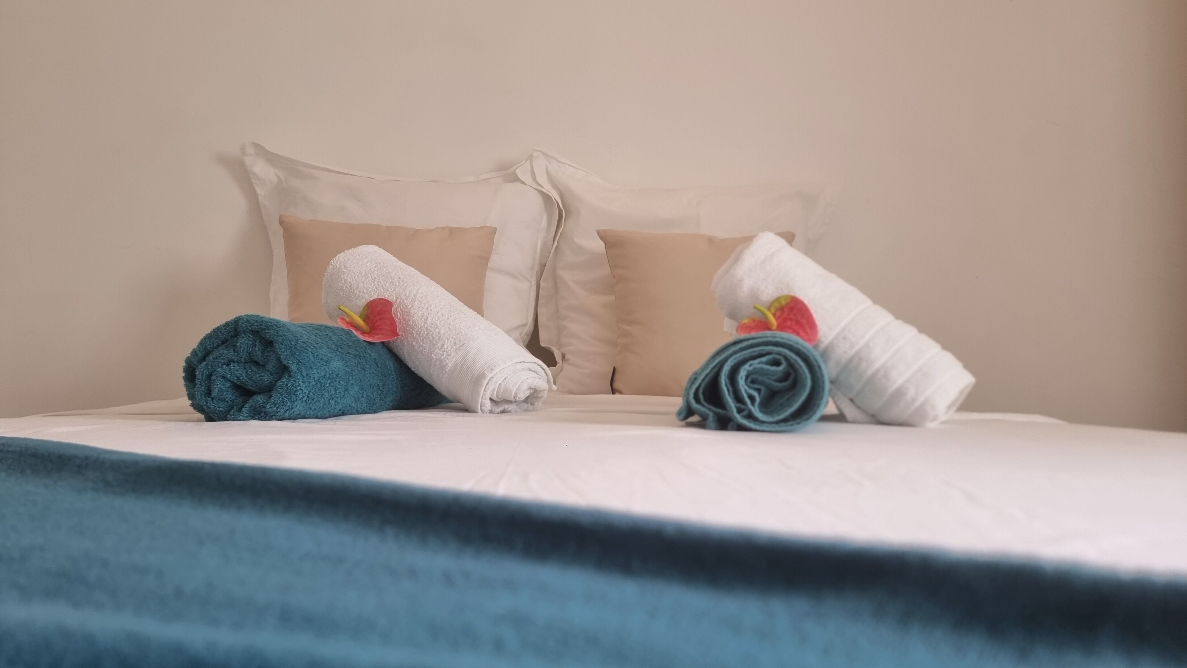 Una cama con una manta azul, dos almohadas y dos toallas enrolladas.