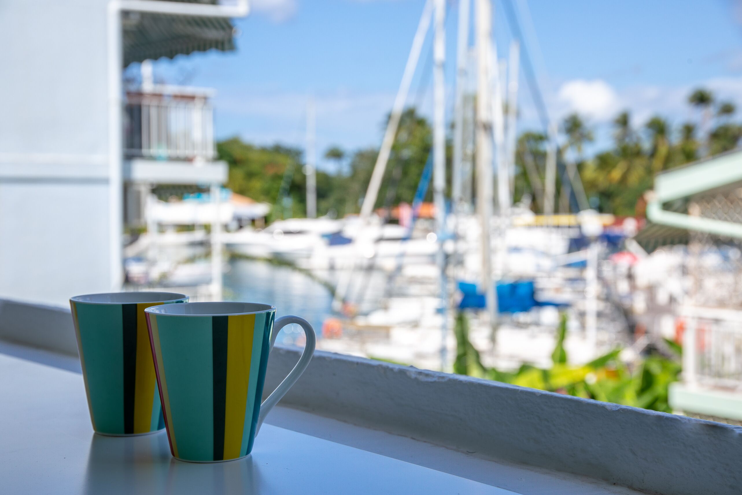 Deux tasses posées sur un rebord de fenêtre, avec vue sur le port de plaisance.