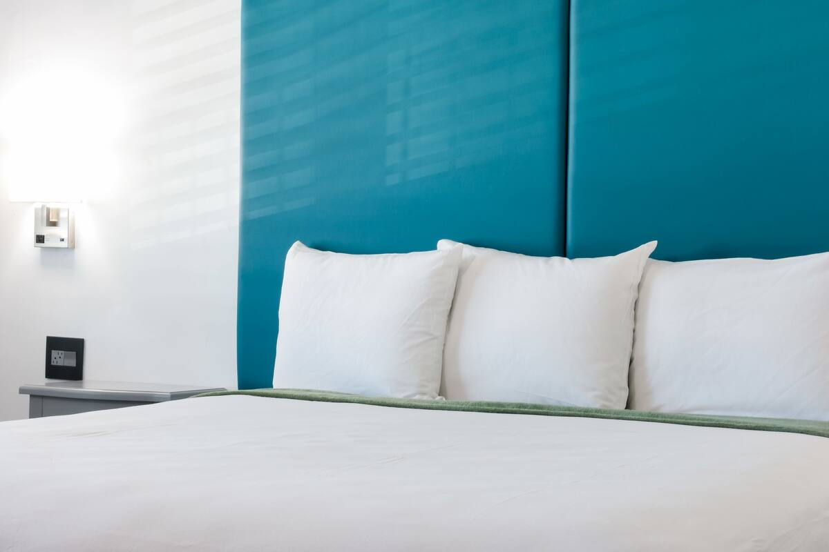 Un lit avec une literie blanche et une tête de lit de couleur turquoise dans une chambre d’hôtel.