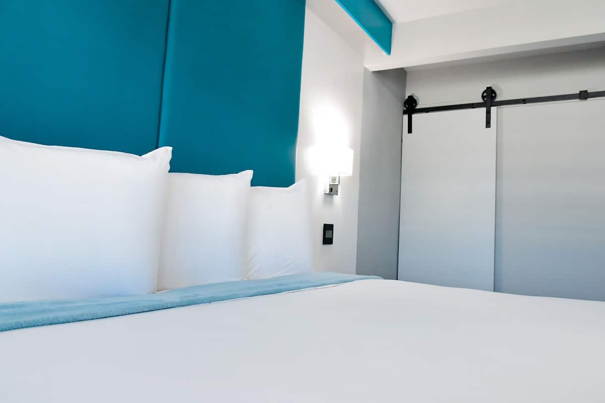 Une chambre d’hôtel moderne avec un grand lit, des murs d’accent de couleur turquoise et un placard à portes coulissantes.