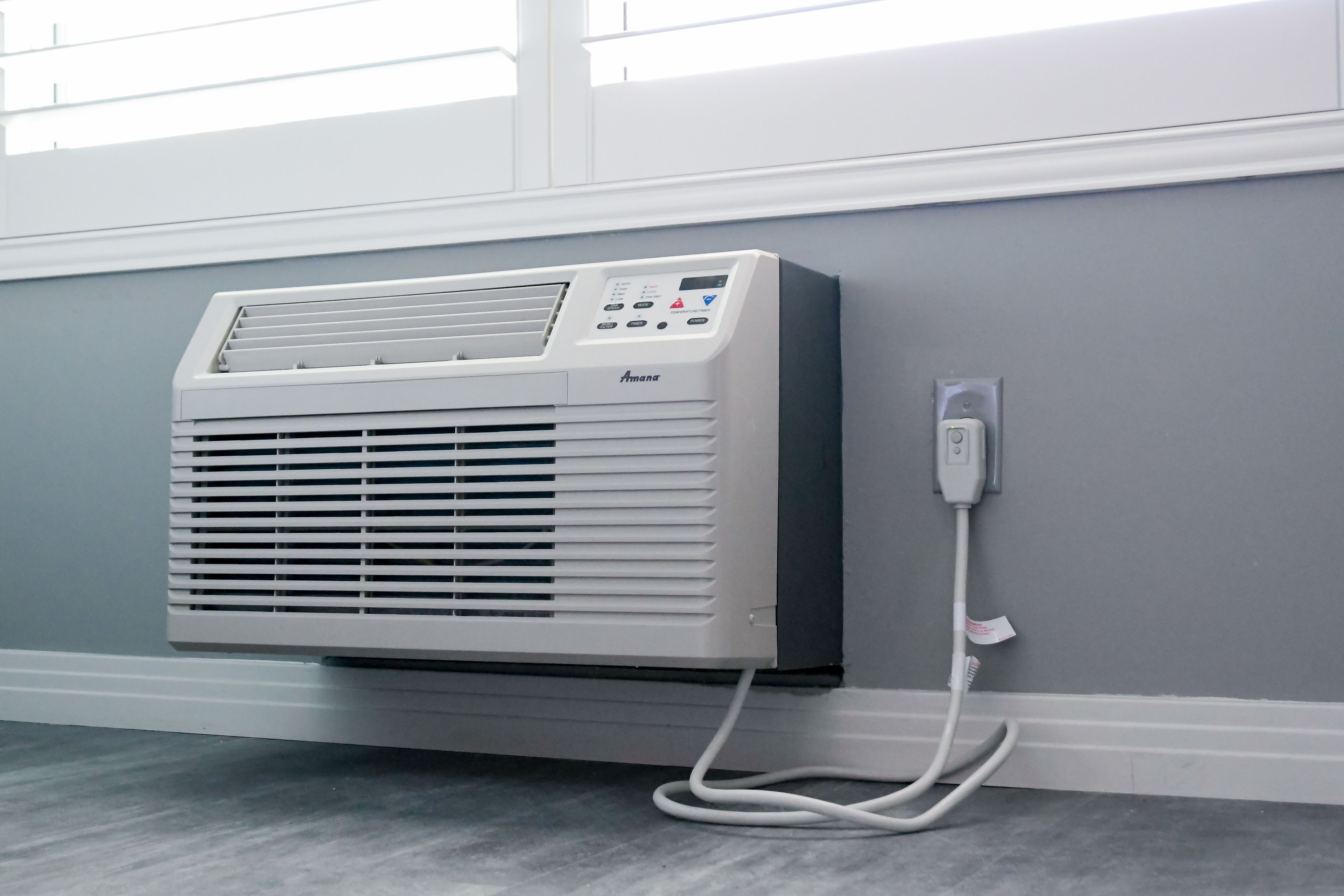 A wall-mounted air conditioner with a control panel and a power cord plugged into a wall socket.