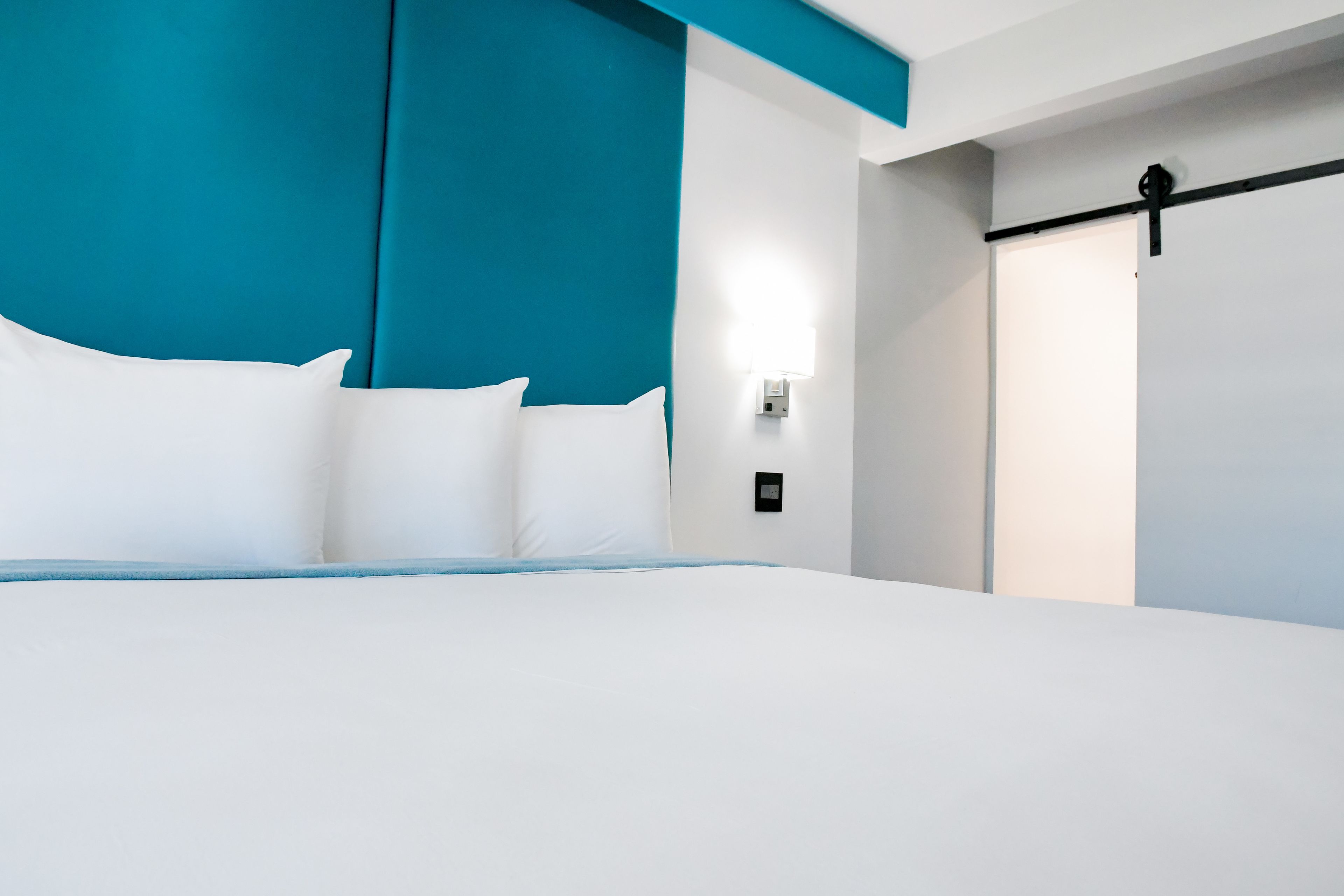 A modern hotel room with a large bed, teal accent walls, and a minimalist design.