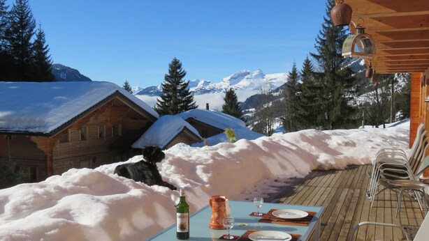 A wooden cabin with a dining table set for two, overlooking a snowy mountain landscape. - Large, sunny, peaceful chalet in the heart of nature in Les Diablerets, Switzerland. (Les Diablerets)