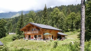 A wooden chalet with a balcony, surrounded by lush greenery and mountains in the background. - Large, sunny, peaceful chalet in the heart of nature in Les Diablerets, Switzerland. (Les Diablerets)