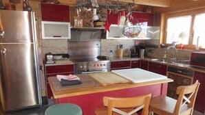 A kitchen with a stainless steel refrigerator, a microwave, a stove, and wooden chairs. - Large, sunny, peaceful chalet in the heart of nature in Les Diablerets, Switzerland. (Les Diablerets)
