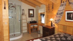 A wooden cabin interior with a glass shower, wooden furniture, and a bed with patterned bedding. - Large, sunny, peaceful chalet in the heart of nature in Les Diablerets, Switzerland. (Les Diablerets)
