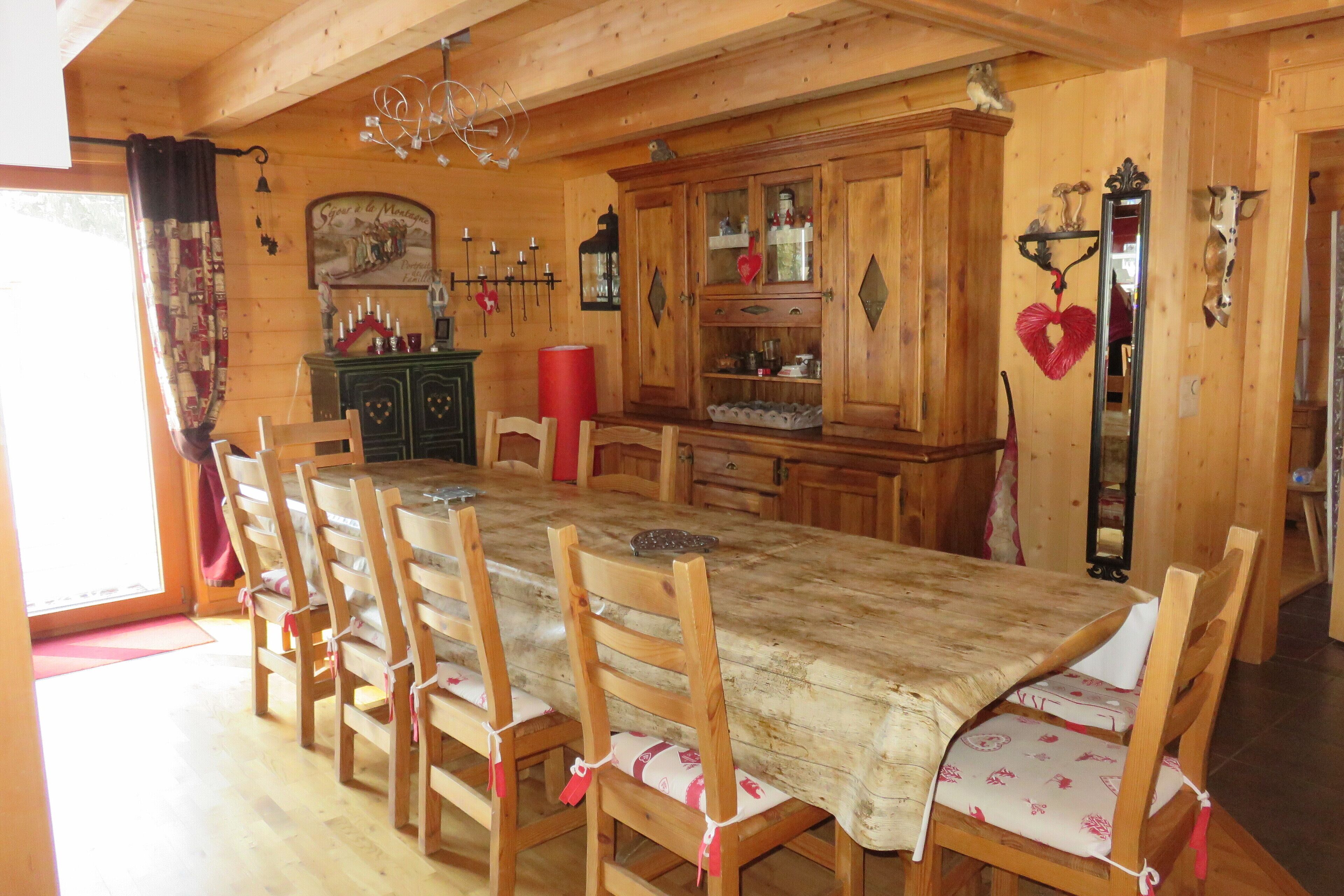 A wooden dining room with a large table and chairs, a cabinet with glass doors, and a mirror.