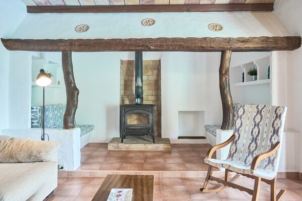 Una sala de estar acogedora con chimenea de piedra, vigas de madera, un sillón estampado y un sofá.