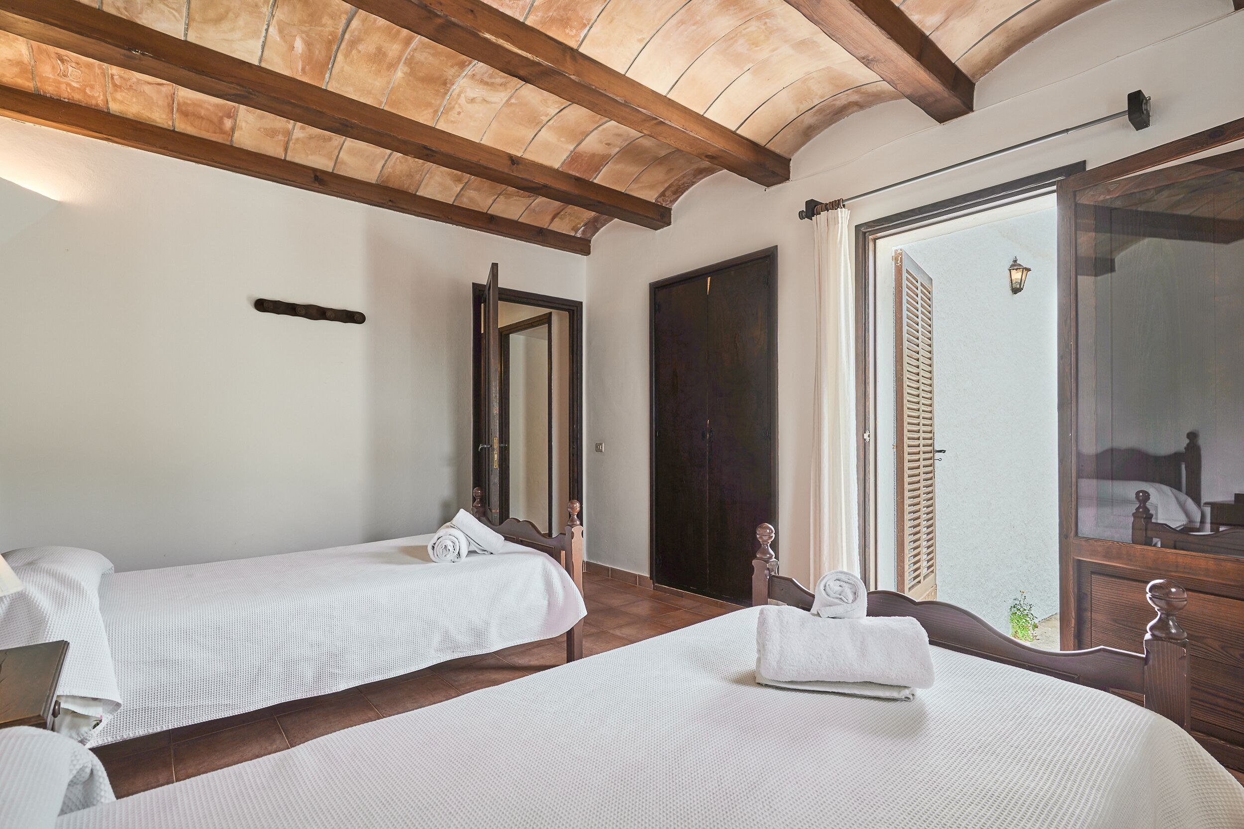 Ein Schlafzimmer mit zwei Einzelbetten, Holz-Kopfteilen, einem großen Spiegel und einer Tür zum Balkon.