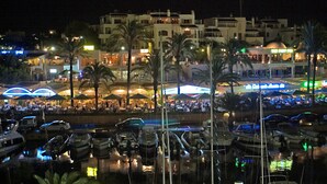 Un port de plaisance avec des bateaux amarrés, une zone de restaurants au bord de l’eau agrémentée de parasols, et des bâtiments en arrière-plan.
