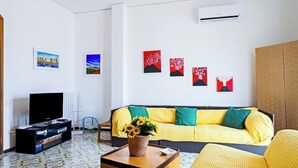 Ein Wohnzimmer mit einer Couch, einem Couchtisch mit Blumenvase, einem Fernseher und Kunstwerken an der Wand.