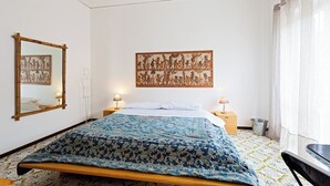 Ein Schlafzimmer mit einem Bett, einem Spiegel, einer Wanddekoration und einem Fenster mit Vorhängen.