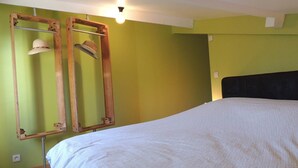 A bedroom with a bed, a wooden headboard, and a mirror with a hat hanging on it. - The Ancient Host (Marcoux)