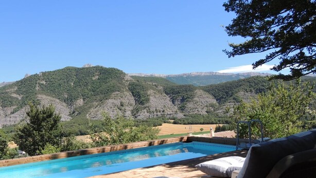 A wooden deck with a pool, lounge chairs, and a view of green hills. - The Ancient Host (Marcoux)
