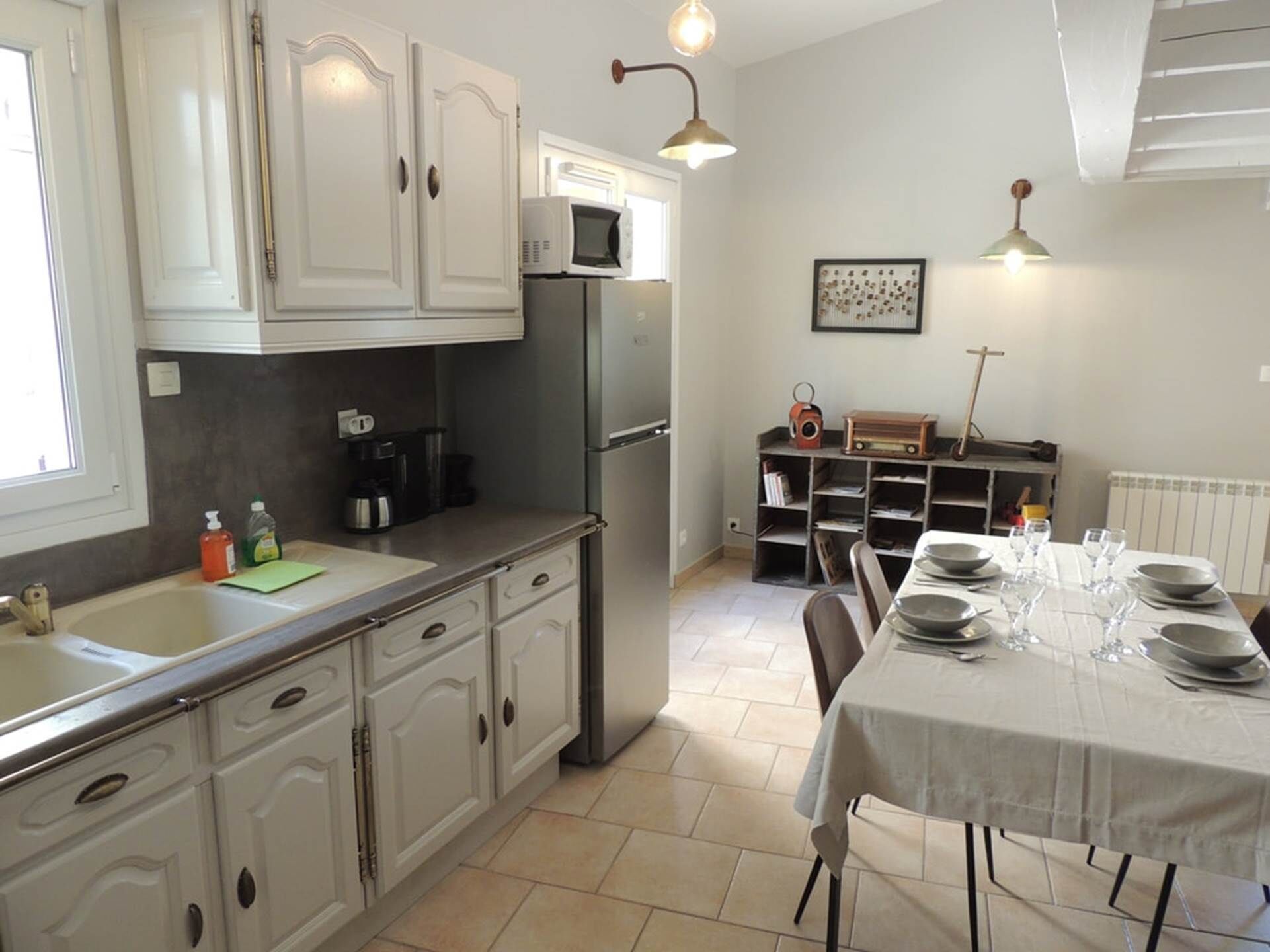 Une cuisine avec des meubles blancs, un réfrigérateur, un four à micro-ondes et une table à manger pour quatre personnes.