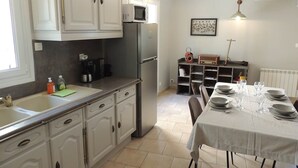 A kitchen with white cabinets, a refrigerator, a microwave, and a dining table set for four. - The Ancient Host (Marcoux)