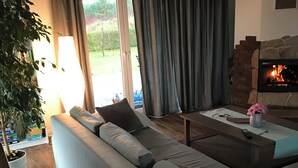 Een moderne woonkamer met een grote bank, een open haard en uitzicht op de omgeving.