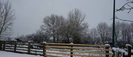 A wooden fence with snow accumulation, a metal post, and bare trees in a snowy landscape.
