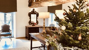 Ein gemütliches Wohnzimmer mit Holzbalkendecke, einem Weihnachtsbaum, einer Couch, einem Tisch und einem Sessel.