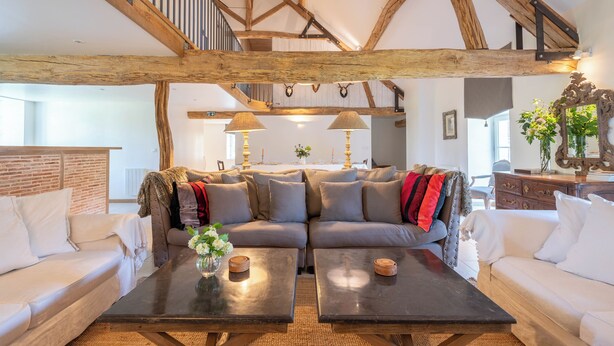 Ein gemütliches Wohnzimmer mit einem großen Ecksofa, zwei Couchtischen und einer Treppe mit freiliegenden Holzbalken.