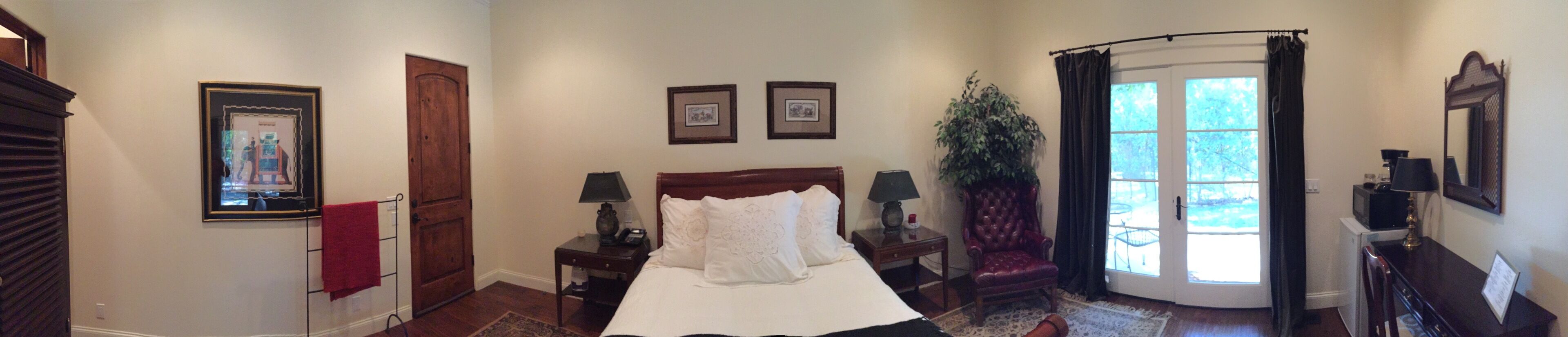 A hotel room with a bed, two bedside tables with lamps, a chair, a large window with curtains, and a door.