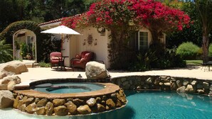 A pool area with a hot tub, surrounded by rocks and a stone wall. There are two chairs and a table under a pergola with red flowers. - Room 4 Two in Montecito/ Santa Barbara (Montecito)