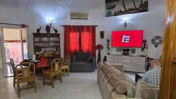 Una sala de estar con televisor, estantería, comedor con sillas y sofá.