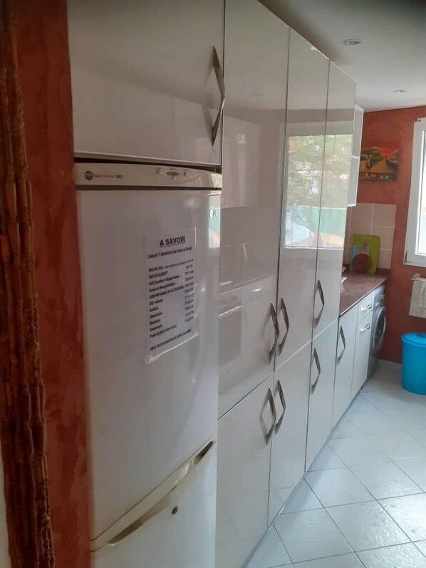 A kitchen with white cabinets, a refrigerator, and a blue trash bin.