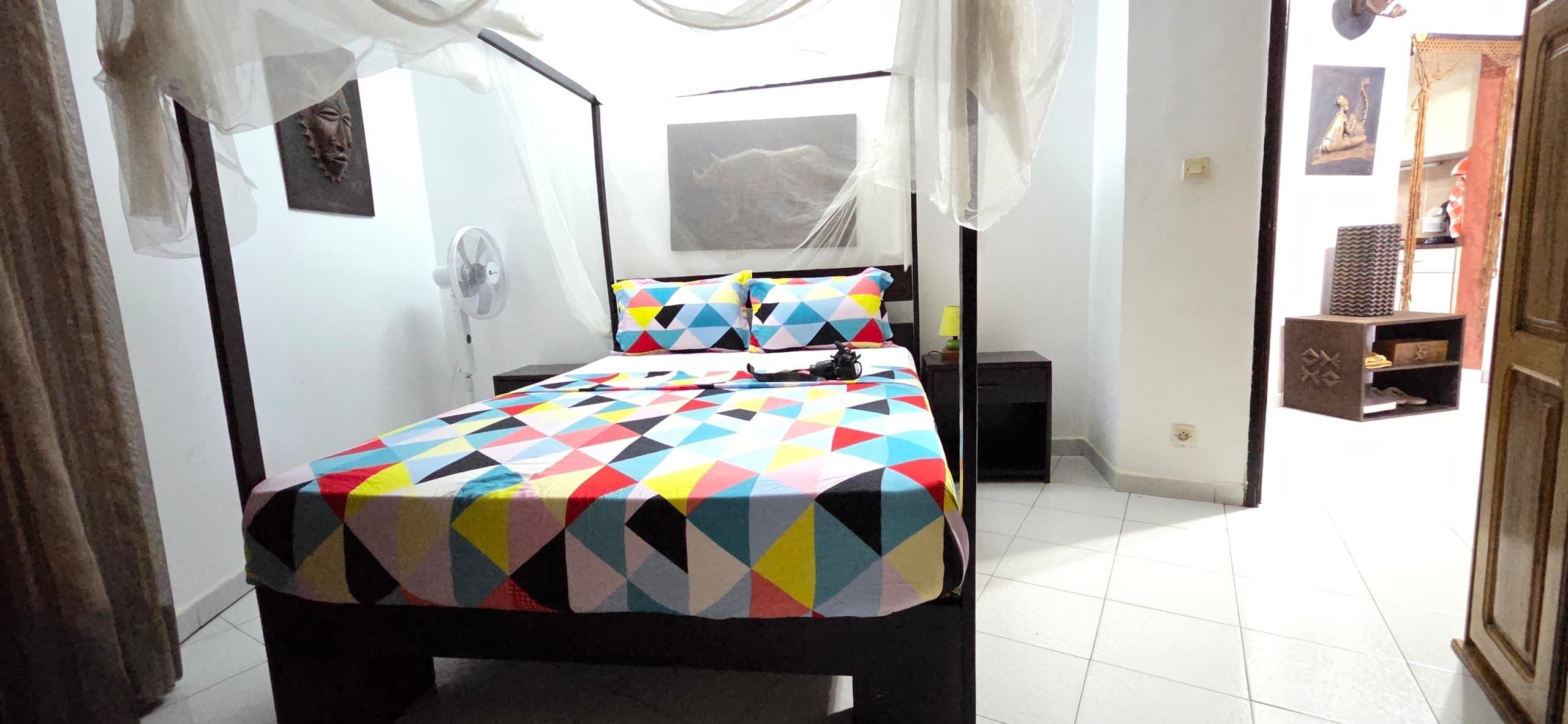 Une chambre à coucher avec un lit, une table de chevet, une lampe et un ventilateur fixé au mur.