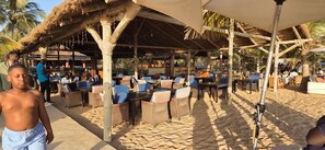 An outdoor seating area with thatched roof structures, wicker furniture, and a sandy ground. - Saly: House / Villa - Saly (Saly)