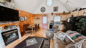 Ein gemütliches Wohnzimmer mit Kamin, Fernseher und Essbereich mit Holzmöbeln.