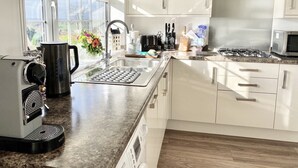 Eine moderne Küche mit weißen Schränken, einer Granitarbeitsplatte, einer Kaffeemaschine, einem Wasserkocher, einer Mikrowelle und einem Gasherd.