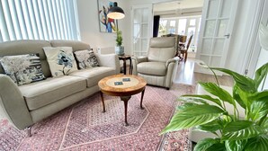 Ein Wohnzimmer mit einem beigen Sofa, einem runden Holztisch und einer großen Zimmerpflanze.