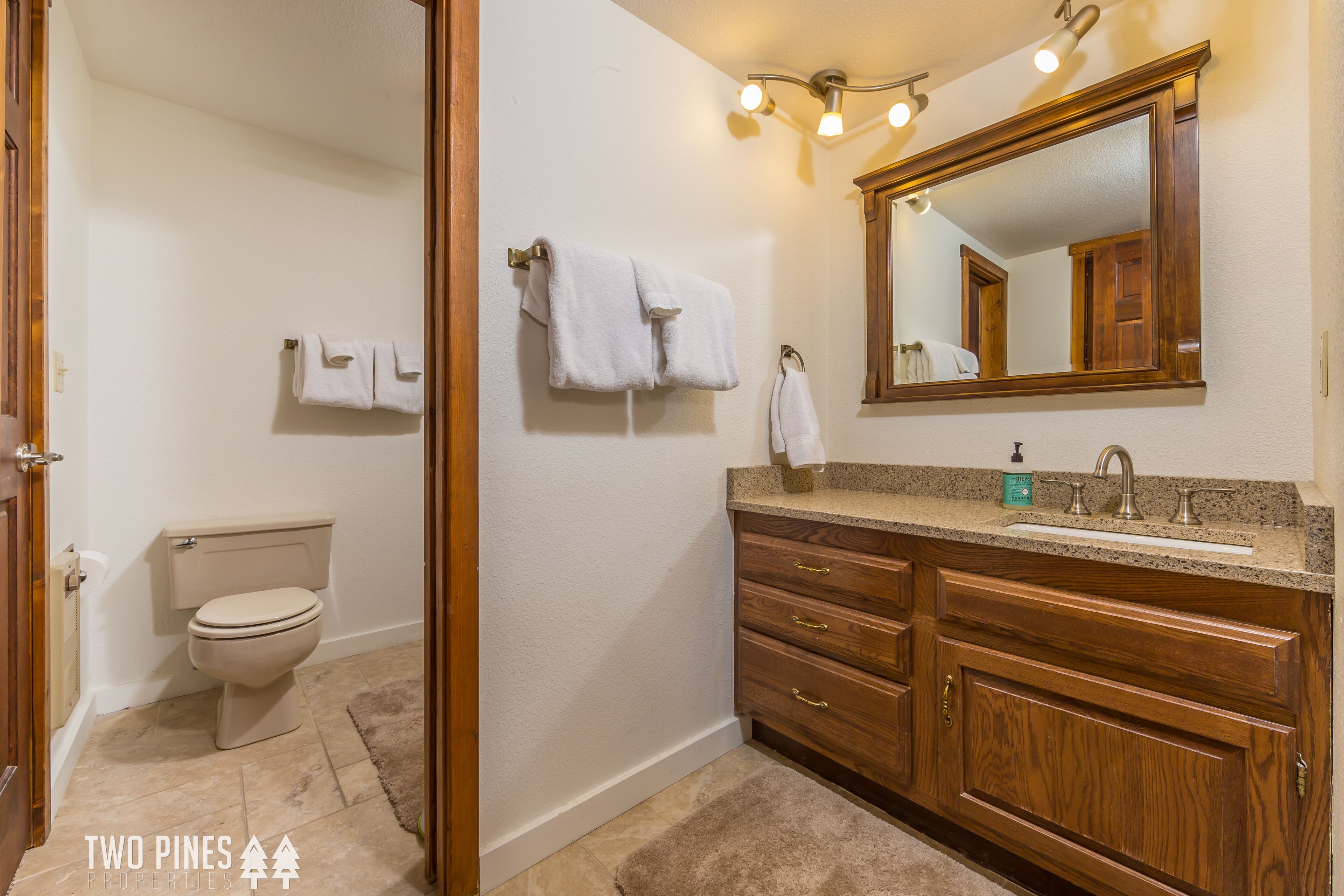 A bathroom with a toilet, wooden vanity, sink, and mirror.