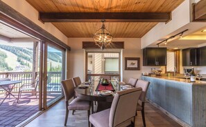 Un comedor con una gran mesa dispuesta para seis personas, una cocina con armarios oscuros y vistas a un paisaje montañoso a través de puertas correderas de vidrio.