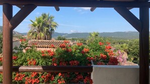 A covered outdoor area with a view of a mountainous landscape, featuring a wooden pergola and lush greenery.