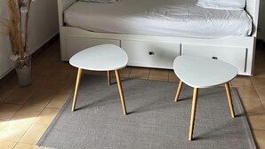 A bedroom with a white bed, two white side tables, a round mirror on the wall, and a vase with pampas grass.