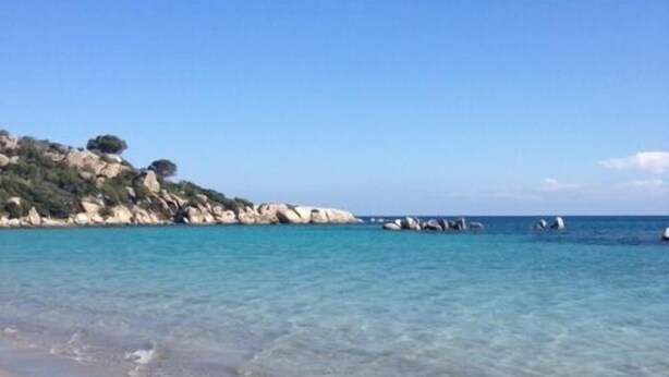 A beach with clear water, sandy shore, rocky outcrops, and a pier.