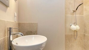 A bathroom with a white vessel sink, a chrome faucet, beige tiled walls, and a shower with a handheld showerhead and a white shower head. - Nice new 2 bedroom town center apartment (Avignon)