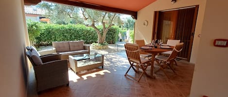Un espace extérieur aménagé en terrasse, avec un canapé, une table à plateau en verre et des chaises.